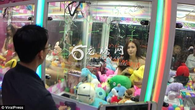 A man attempts to win a prize from an arcade claw game with a bikini-clad model inside