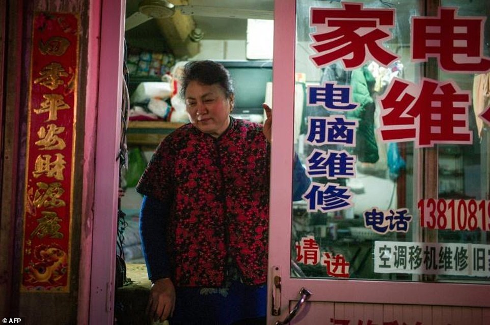 The narrow streets bustle with activity from food stalls shops and the constant flow of bikes and motorcycles. Pictured is the wife of Gu Chen an electrical appliance repairman residing in hutong. She stands in front of the one-room apartment where she and her husband have slept and worked in all her life