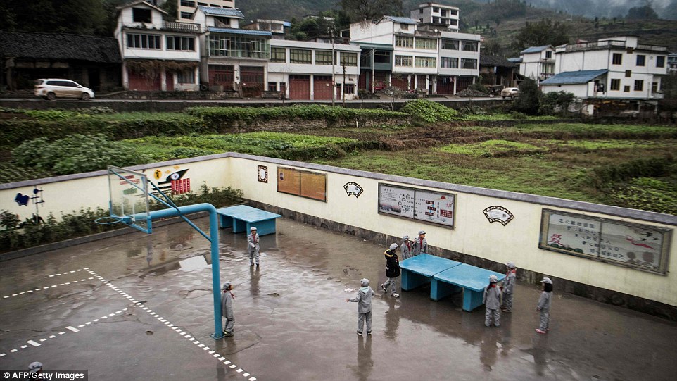 Children gather around a ping pong table in the rain-soaked playground