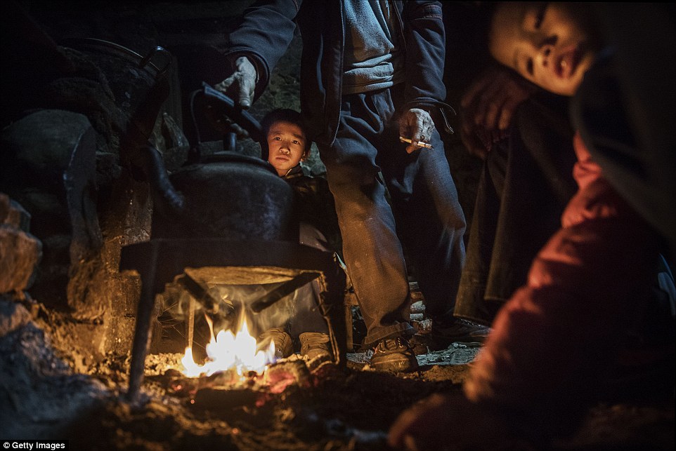 'Left behind' child  Luo Gan 10(centre) stays warm by a fire at the family house