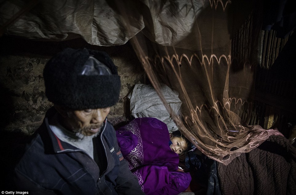 Grandfather Luo Yingtao 64 sits next to his grandson 'left behind' child Luo Lie five as he puts him to bed at the family house in Anshun China