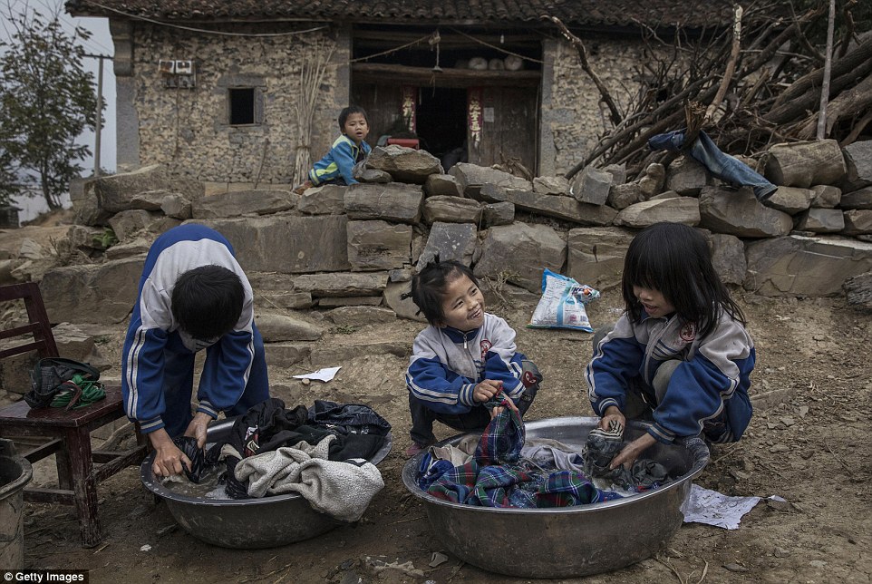 'Left behind' child Luo Hongniu eight (centre) washes clothes with brother Luo Gan 10 and sister Luo Hongni 11 (right) outside the family house in Anshun