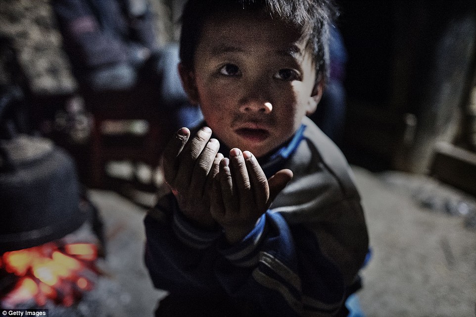 'Left behind' child Luo Lie five keeps warm by a fire in the family home. He is one of millions of children whose parents have migrated to urban areas