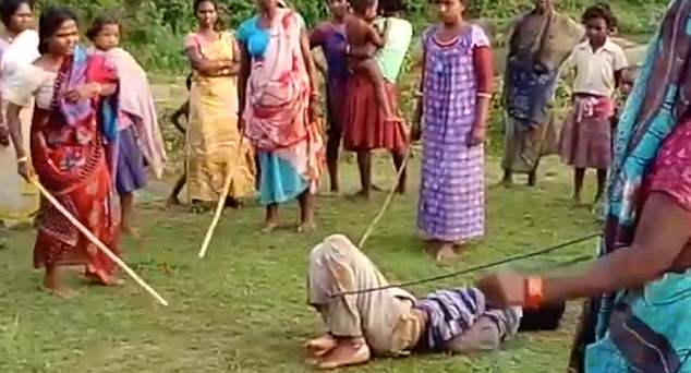 Dozens of women and children look on as the women take turns hitting the man with long sticks