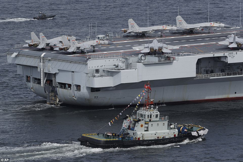 The Liaoning was accompanied by two destroyers and other ships from its strike group with jet fighters and helicopters visible on the flight deck alongside hundreds of crew dressed in white uniforms